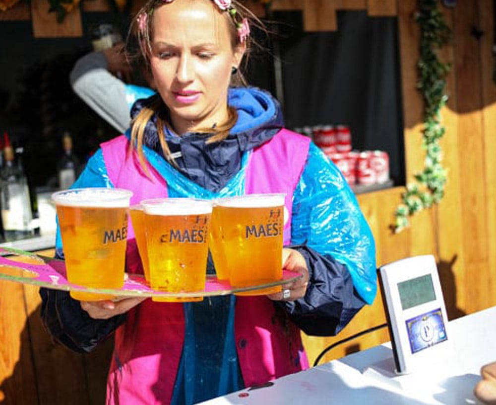 A woman holds a tray of beers next to a cashless payment terminal