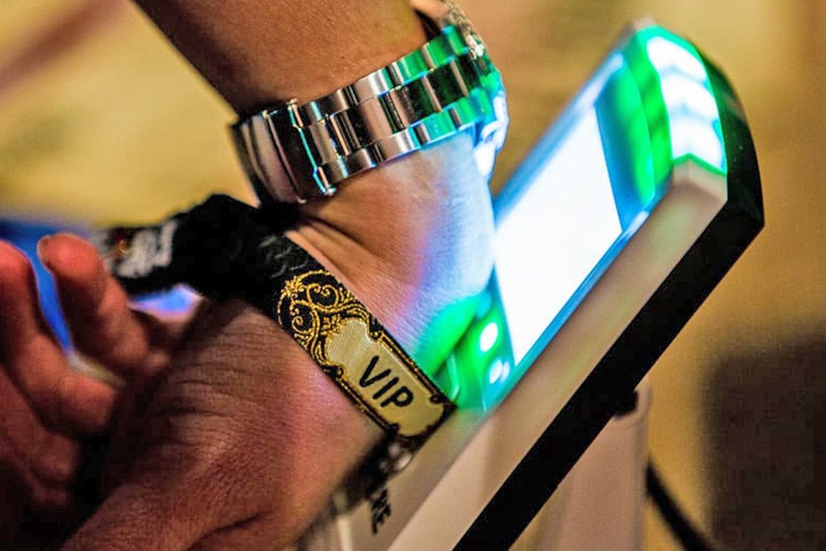 A closeup of an attendees wrist with an RFID wristband scanning a reader.